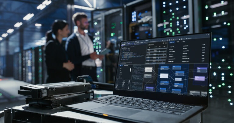 Data center environment with laptop and hard drives as two professionals discuss network infrastructure and server maintenance among server racks